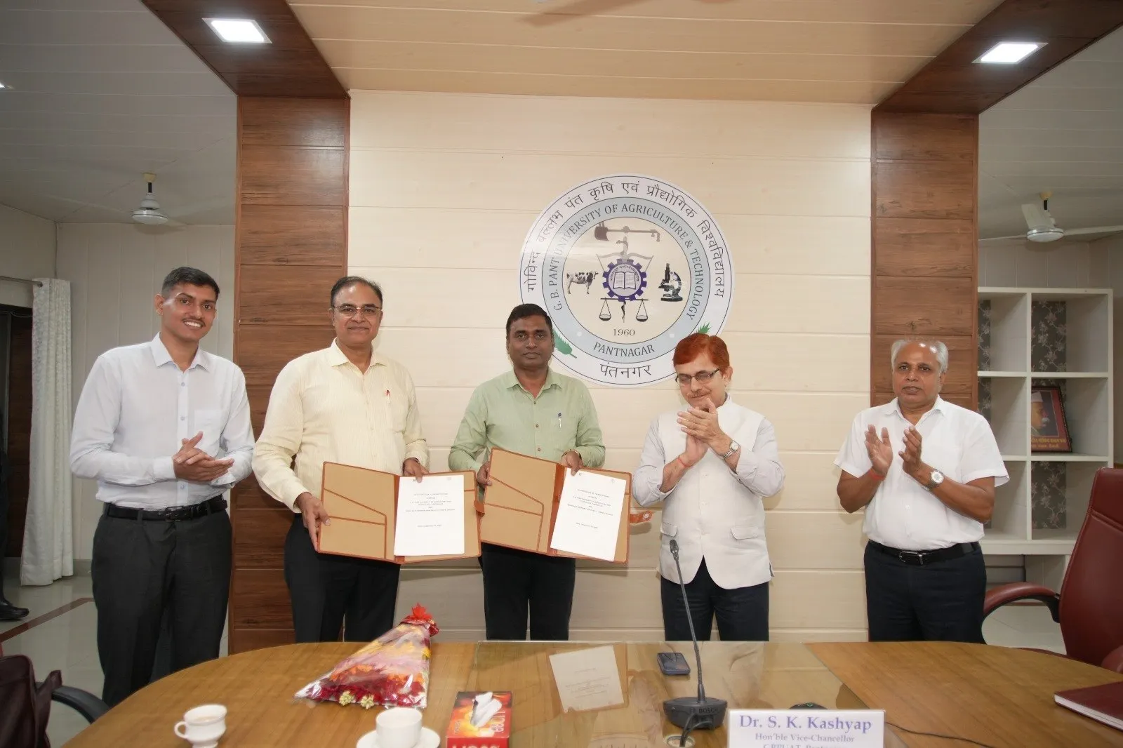 The MoU signing at G.B. Pant University of Agriculture & Technology, Pantnagar: the Director Research and Rajeev Tomer hold the signed folders beneath the University crest, with the Vice-Chancellor Dr. S. K. Kashyap and other officials alongside.